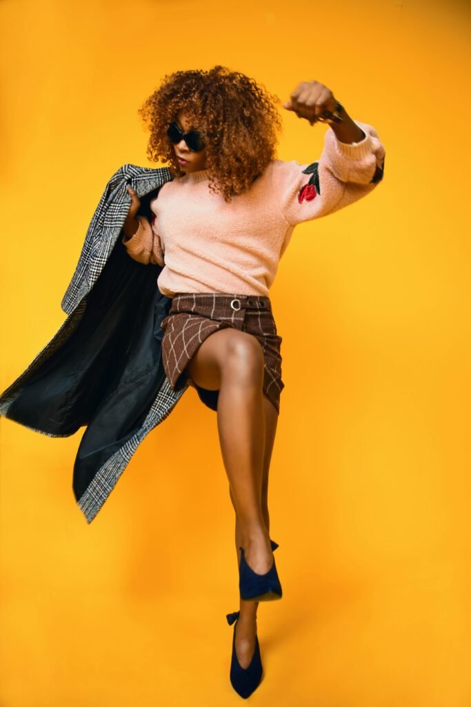 Stylish woman in a dynamic fashion pose against a vibrant orange background.